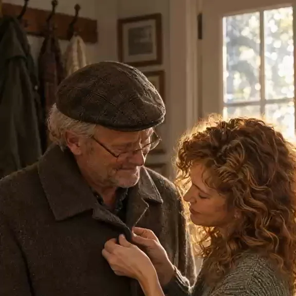 A daughter buttons her father's coat while he smiles down at her, his cane in his other hand.